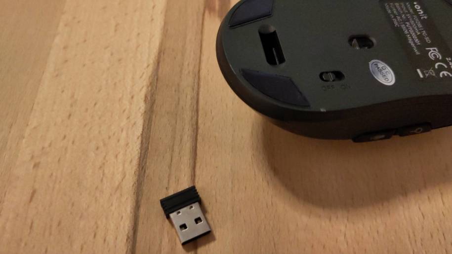 Die onit Maus liegt auf dem Rücken, man sieht den leeren Dongle-Steckplatz, daneben liegt der kleine USB-Dongle