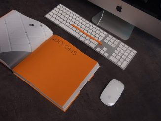 Ein Mac der auf einem Tisch steht, mit einem Buch davor